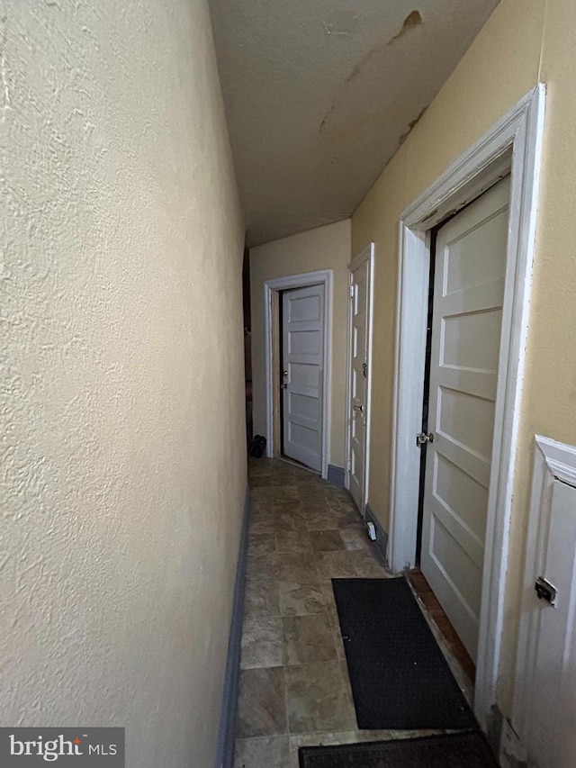 hallway featuring a textured wall and baseboards