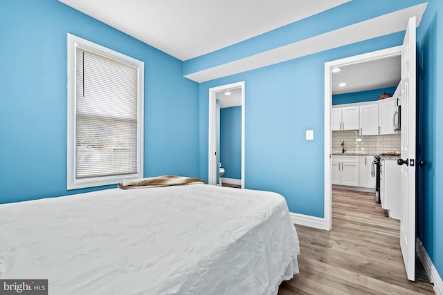 bedroom featuring connected bathroom, sink, and light hardwood / wood-style flooring