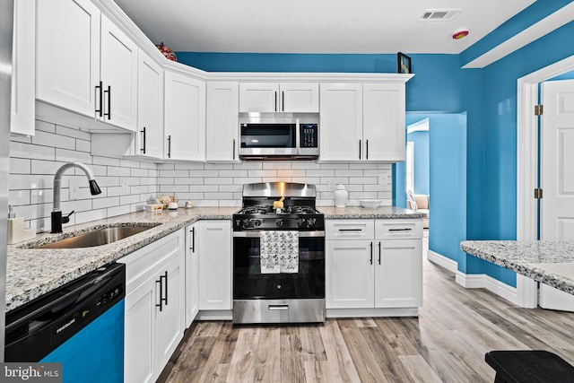 kitchen featuring sink, light stone counters, appliances with stainless steel finishes, light hardwood / wood-style floors, and white cabinets