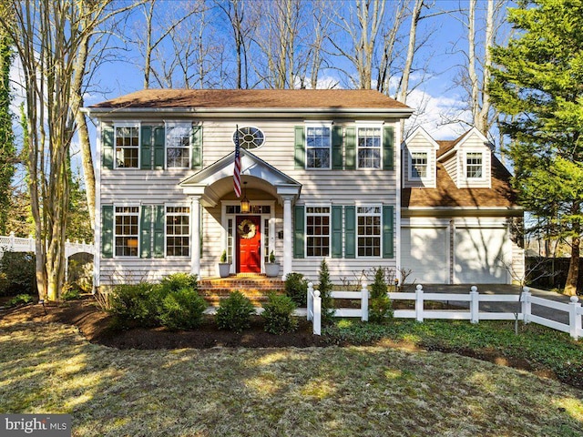 colonial inspired home featuring an attached garage and a fenced front yard