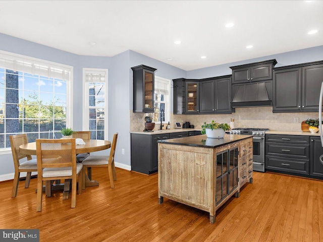 kitchen featuring custom exhaust hood, light wood-style floors, tasteful backsplash, and stainless steel range with gas cooktop