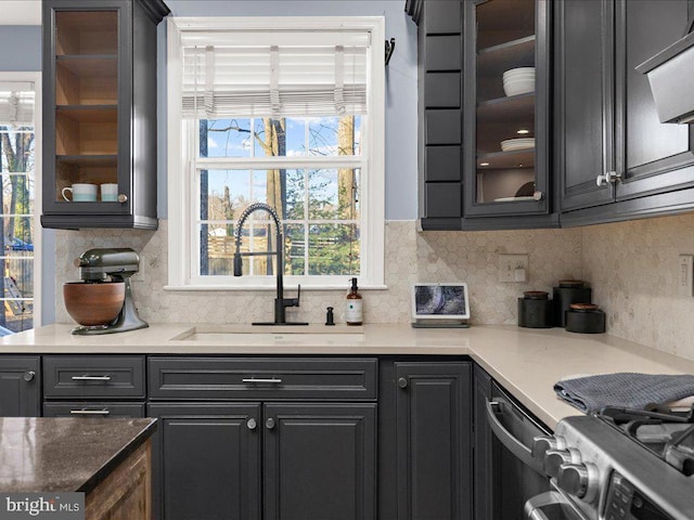 kitchen featuring a sink, backsplash, glass insert cabinets, light stone countertops, and stainless steel gas range