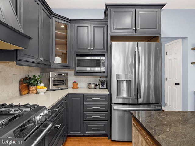 kitchen with tasteful backsplash, glass insert cabinets, wall chimney range hood, a toaster, and appliances with stainless steel finishes