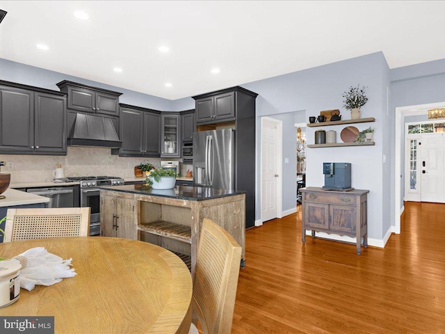 kitchen featuring backsplash, glass insert cabinets, wood finished floors, custom exhaust hood, and stainless steel appliances