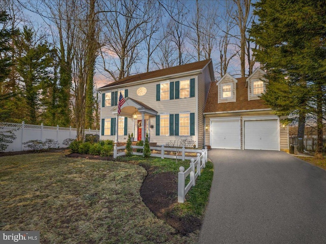 colonial house with an attached garage, driveway, a fenced front yard, and a yard