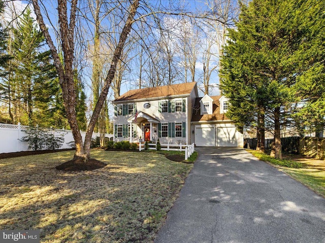 colonial-style house with fence, driveway, an outdoor structure, a front lawn, and a garage