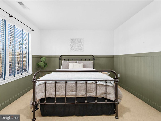 carpeted bedroom with visible vents and a wainscoted wall