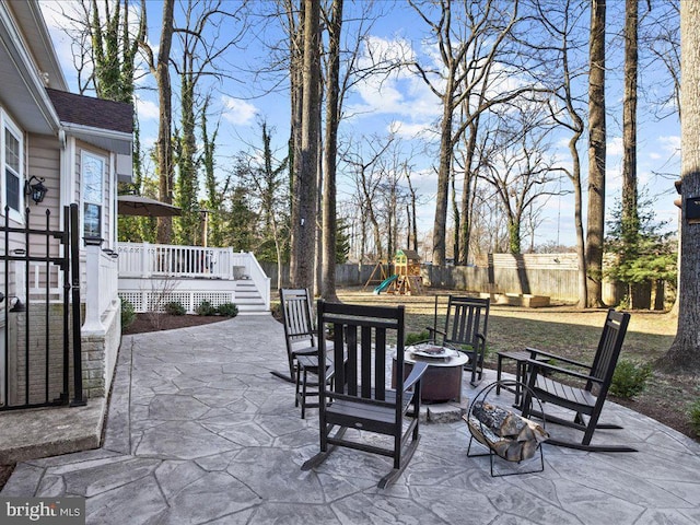 view of patio featuring a deck, an outdoor fire pit, a playground, and a fenced backyard