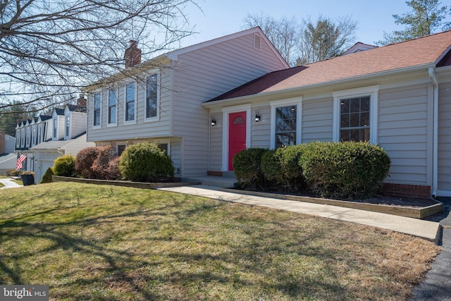 tri-level home with a shingled roof, a chimney, and a front lawn