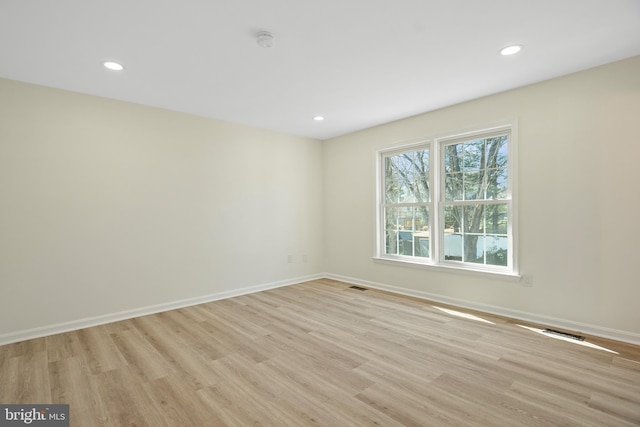 spare room featuring light wood finished floors, visible vents, and baseboards