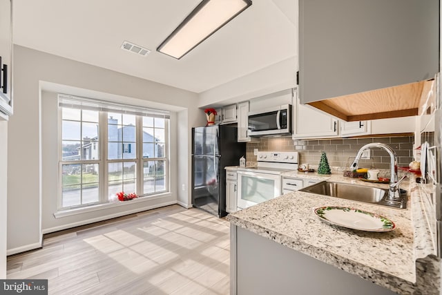 kitchen featuring sink, white cabinetry, backsplash, black refrigerator, and white electric range oven