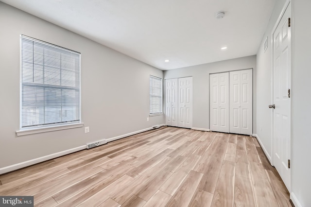 unfurnished bedroom featuring light hardwood / wood-style flooring and two closets