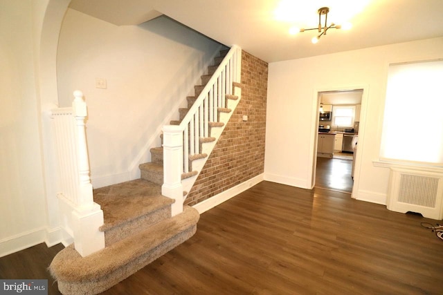 stairway featuring wood-type flooring, brick wall, radiator, and a notable chandelier