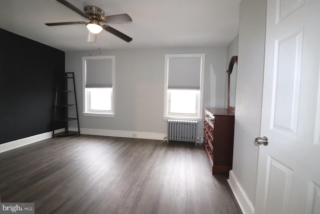 unfurnished bedroom with multiple windows, ceiling fan, radiator, and dark hardwood / wood-style floors