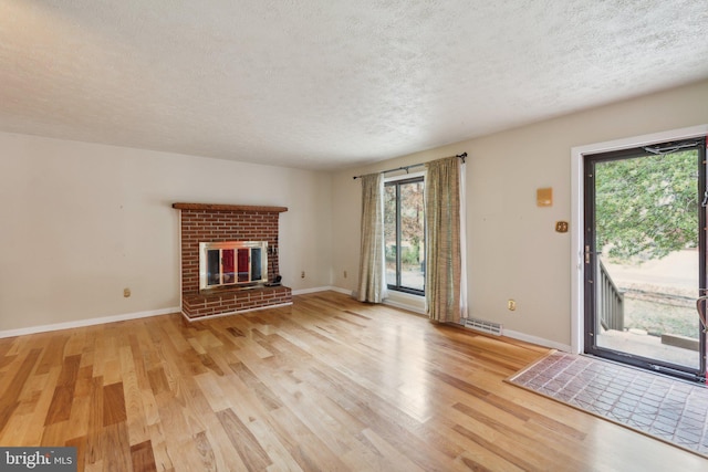 unfurnished living room with light hardwood / wood-style floors, a brick fireplace, and a textured ceiling