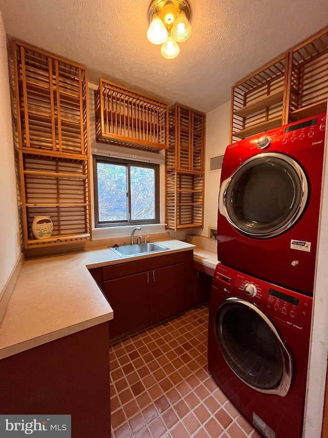 laundry room with stacked washer and dryer, cabinets, sink, and a textured ceiling