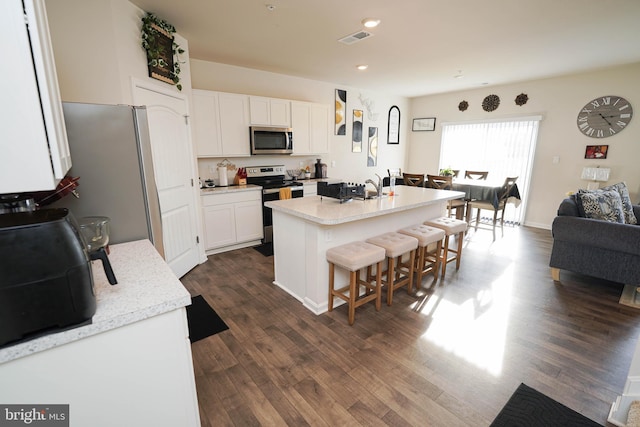 kitchen featuring a breakfast bar area, white cabinetry, a center island with sink, appliances with stainless steel finishes, and dark hardwood / wood-style flooring