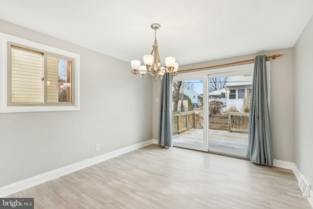 unfurnished dining area featuring a chandelier, light wood-style flooring, and baseboards