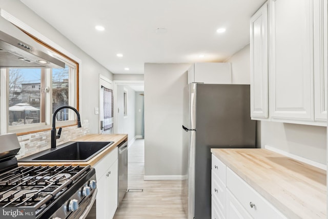 kitchen featuring decorative backsplash, appliances with stainless steel finishes, light wood-style floors, white cabinets, and a sink