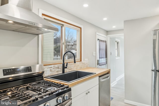 kitchen featuring tasteful backsplash, butcher block counters, appliances with stainless steel finishes, ventilation hood, and a sink