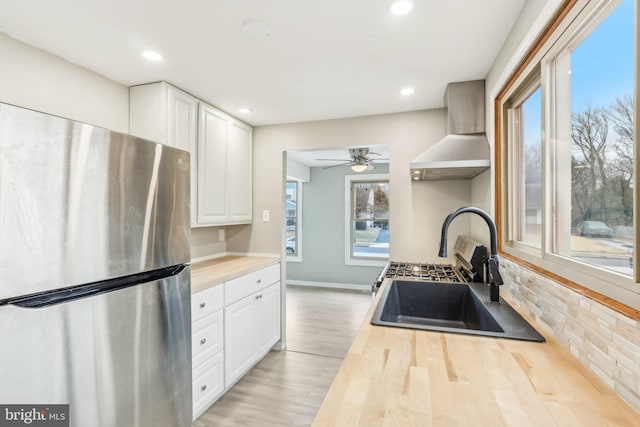 kitchen featuring wall chimney exhaust hood, butcher block countertops, a sink, and freestanding refrigerator