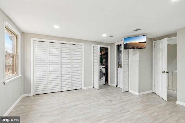 unfurnished bedroom with wood finished floors, visible vents, baseboards, two closets, and washer / dryer