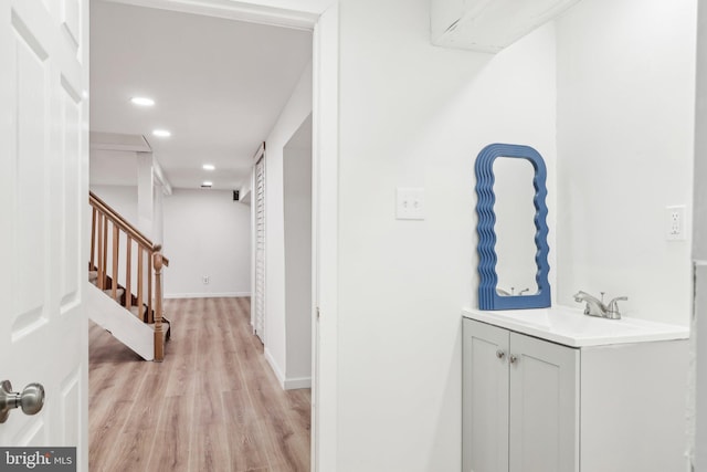 corridor featuring recessed lighting, a sink, baseboards, stairs, and light wood finished floors