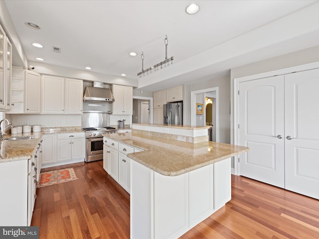 kitchen featuring wall chimney exhaust hood, a kitchen island, glass insert cabinets, stainless steel appliances, and white cabinetry