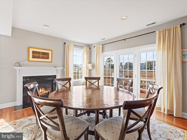 dining space featuring a fireplace with flush hearth, visible vents, baseboards, and wood finished floors