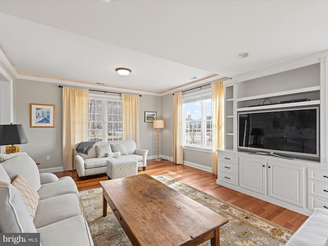 living area with ornamental molding, light wood-style flooring, and baseboards