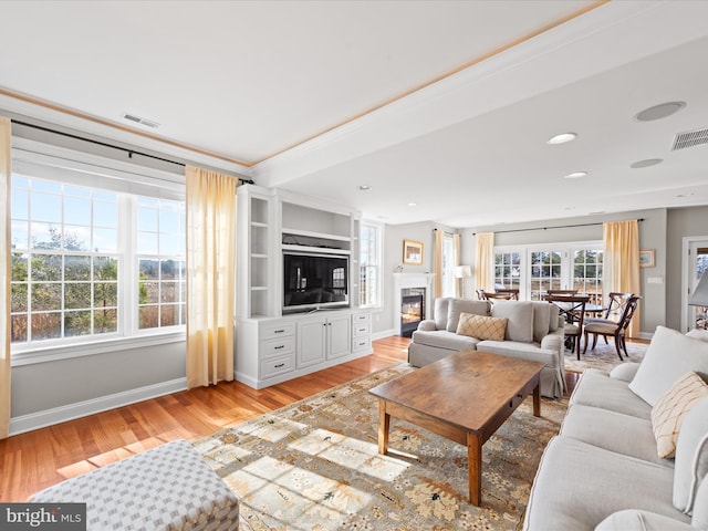 living area with light wood finished floors, a glass covered fireplace, visible vents, and baseboards