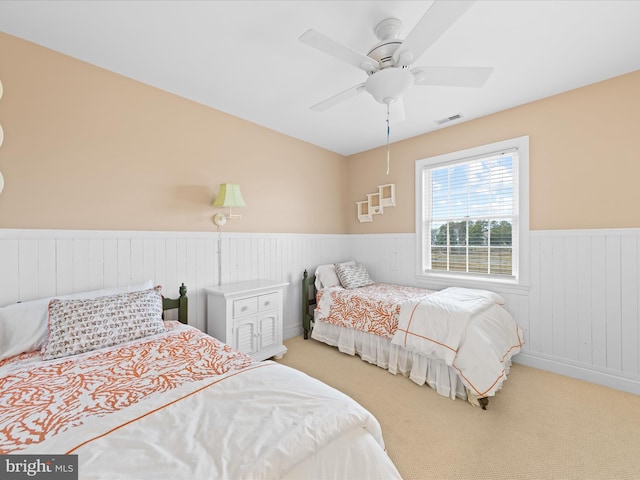 carpeted bedroom with a ceiling fan, wainscoting, and visible vents