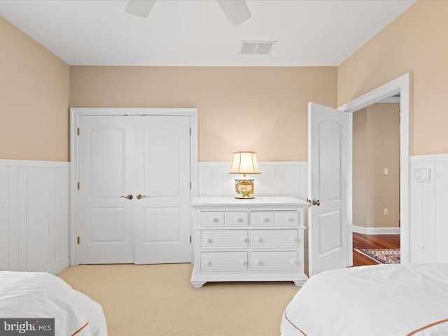 bedroom with a wainscoted wall, visible vents, and a ceiling fan