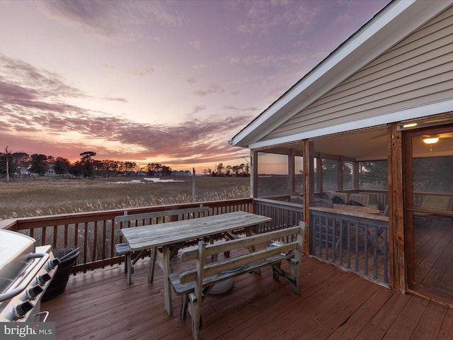 deck at dusk with outdoor dining space and a sunroom