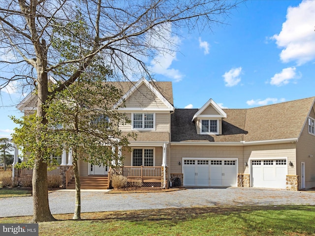 view of front of home with an attached garage, covered porch, a shingled roof, driveway, and stone siding