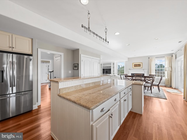 kitchen featuring stainless steel fridge with ice dispenser, light wood-style flooring, open floor plan, a center island, and a fireplace