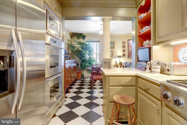 kitchen featuring ornamental molding, dark floors, stainless steel appliances, decorative columns, and cream cabinets