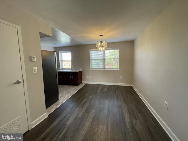 unfurnished dining area featuring a healthy amount of sunlight, dark wood-type flooring, and a notable chandelier