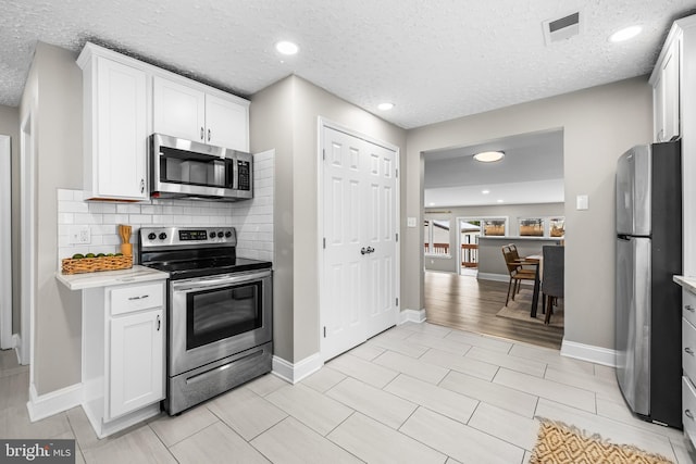 kitchen featuring stainless steel appliances, white cabinetry, and tasteful backsplash