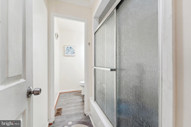 full bath with visible vents, toilet, a shower with shower door, wood finished floors, and baseboards