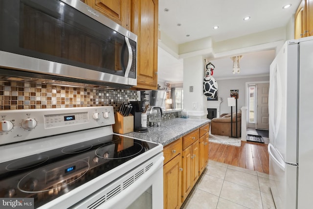 kitchen featuring light tile patterned floors, white appliances, a fireplace, tasteful backsplash, and crown molding