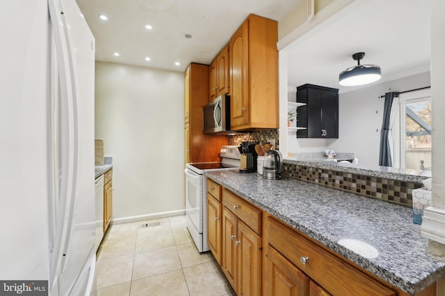 kitchen featuring stone counters, brown cabinets, light tile patterned floors, decorative backsplash, and white appliances