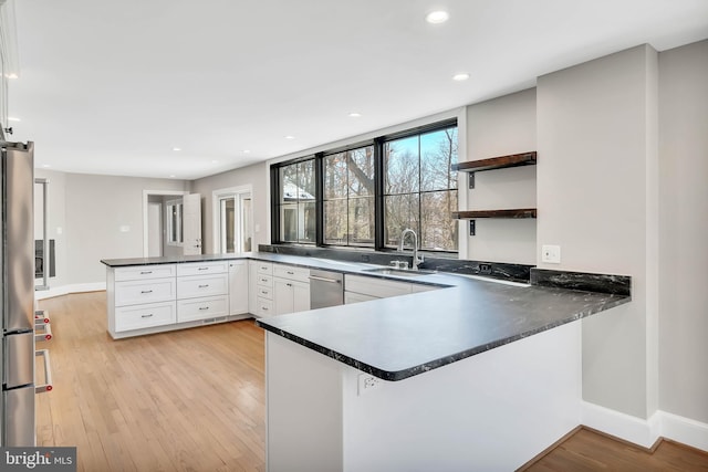 kitchen featuring appliances with stainless steel finishes, white cabinetry, sink, kitchen peninsula, and light wood-type flooring