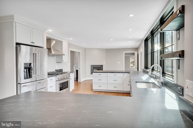 kitchen with white cabinetry, sink, high end appliances, wall chimney exhaust hood, and light hardwood / wood-style flooring