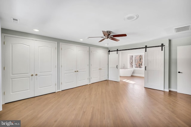 unfurnished bedroom featuring multiple closets, ceiling fan, a barn door, and light hardwood / wood-style floors