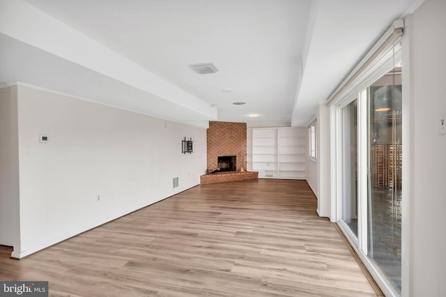 unfurnished living room with a brick fireplace, built in features, and light wood-type flooring