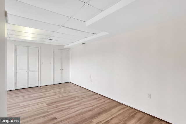 unfurnished bedroom with multiple closets, a paneled ceiling, and light hardwood / wood-style floors