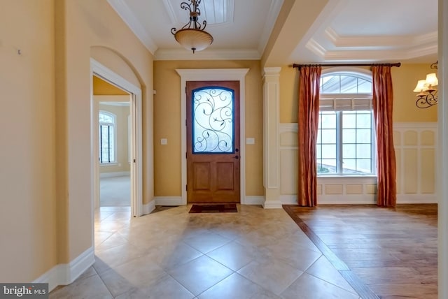 foyer entrance featuring ornamental molding, light tile patterned flooring, an inviting chandelier, and a tray ceiling