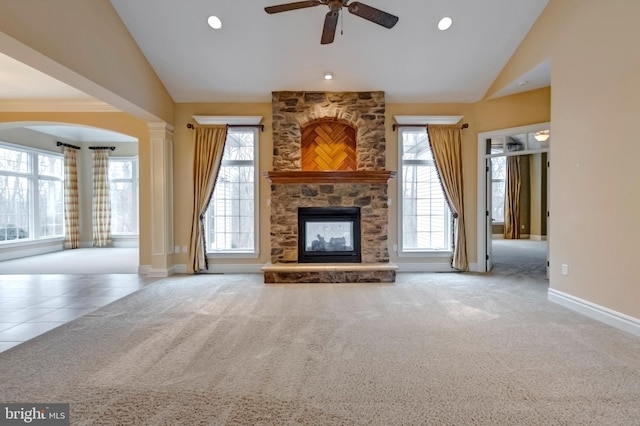 unfurnished living room featuring ornate columns, a wealth of natural light, a stone fireplace, and light carpet