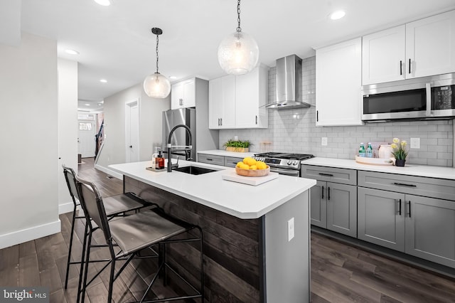 kitchen featuring a center island with sink, wall chimney exhaust hood, appliances with stainless steel finishes, dark wood-type flooring, and gray cabinets